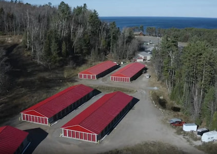 Bird's eye view of several large red warehouses in a forest by a large body of water.
